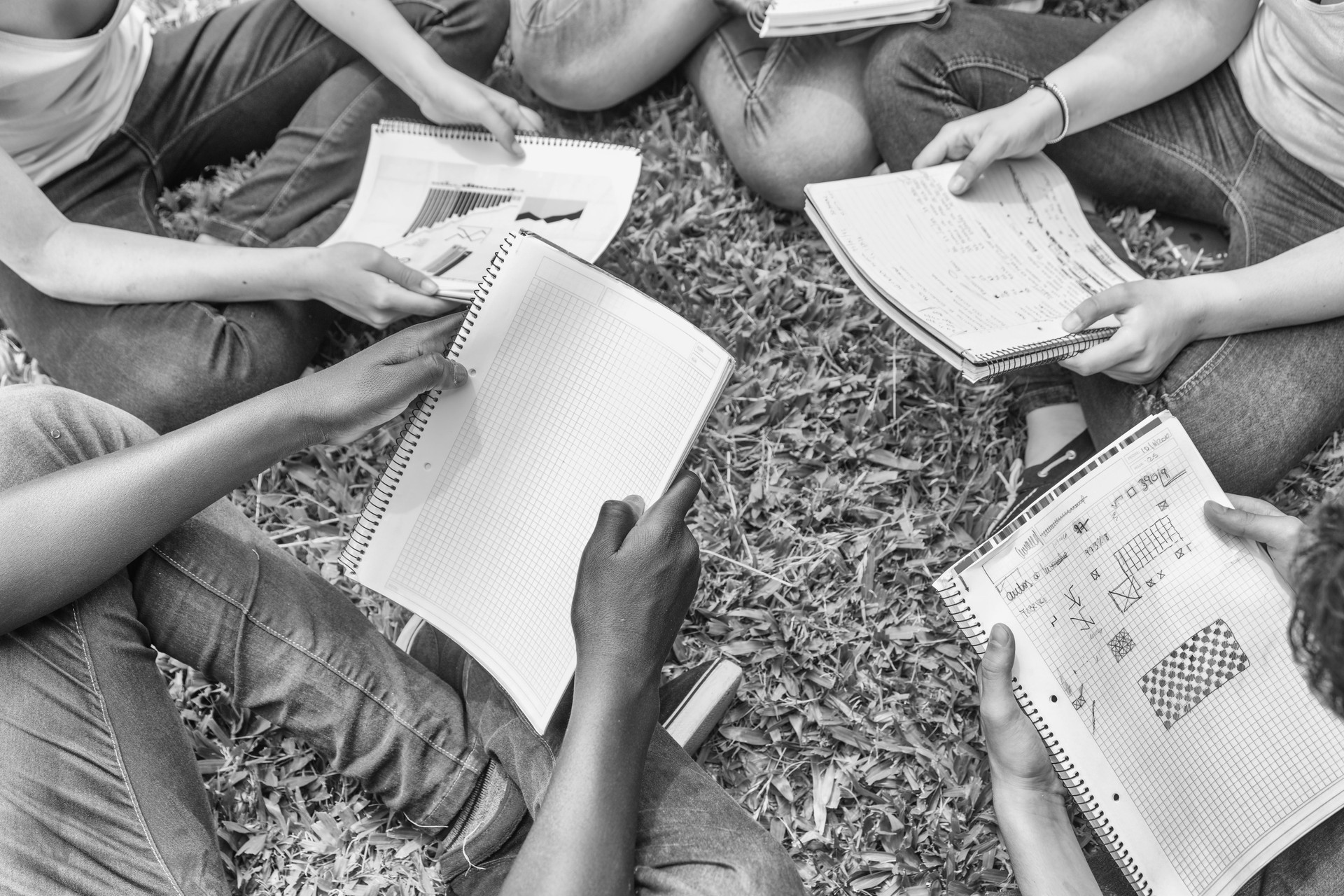 Group of teenagers making school tasks seated on the grass. School and friendship concept. Notebooks detail
